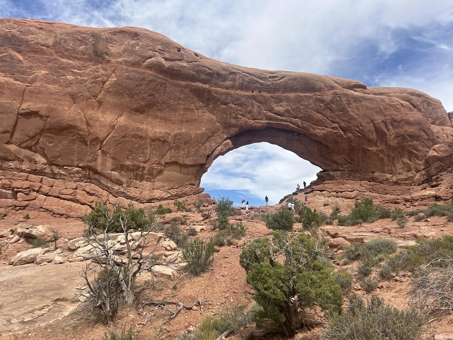 Classic arch rock formation with people climbing on it in the distance